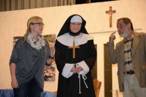 Theaterszene: Drei Darsteller im Dialog - junge Frau, Nonne und älterer Mann