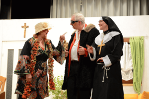 Theaterdialog zwischen Person im Kimono, Showmaster-Figur und Nonne bei heiterer Szene